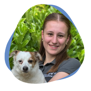 Junge Frau mit grauem Poloshirt, braunen Haaren und Hund auf dem Arm