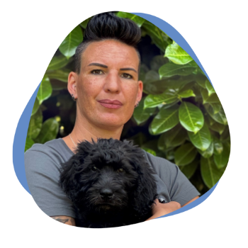 Frau mit kurzen dunklen Haaren und einem schwarzen Hund auf dem Arm